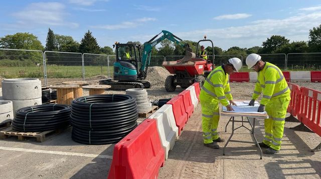 Operatives reviewing utility plans beside staged ducting and a separated plant zone on a UK civils site